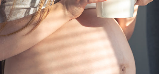 Zwangere vrouw houdt kopje raspberry Leaf tea vast om bevalling natuurlijk te starten.