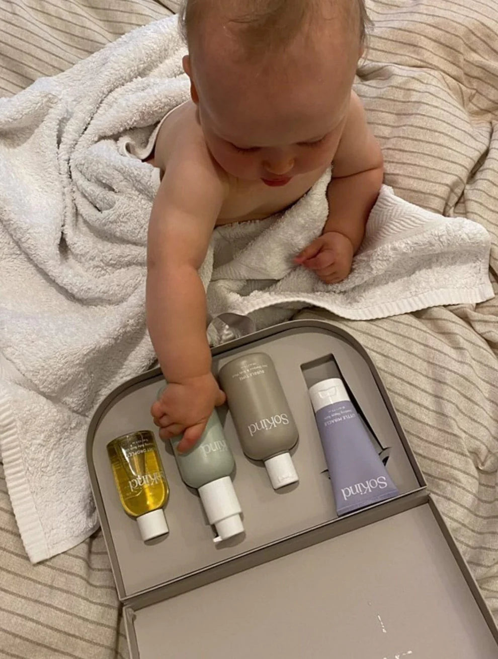 Een baby die recht zit voor het koffertje met verzorgingsproducten van SoKind en één product vastneemt om eruit te halen.