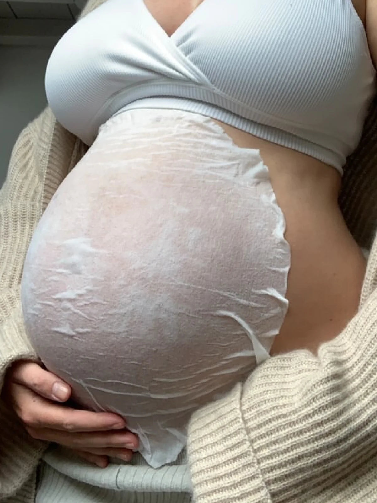 Zwangere vrouw die het Blissful Moment Belly Sheet Mask van SoKind uit de Pregnancy Skin Care Kit op haar buik legt.