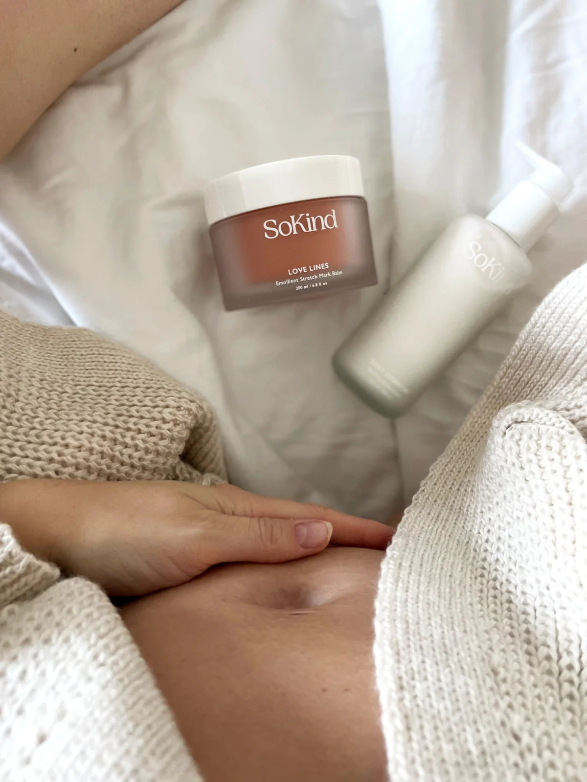 Een zwangere vrouw die van bovenaanzicht een foto heeft genomen van haar buik met de Love Lines van Sokind uit de Pregnancy Skin Care Kit ernaast.