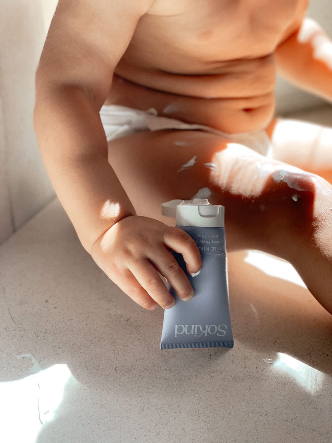 Een baby houdt de Little Miracle luierzalf van SoKind vast.