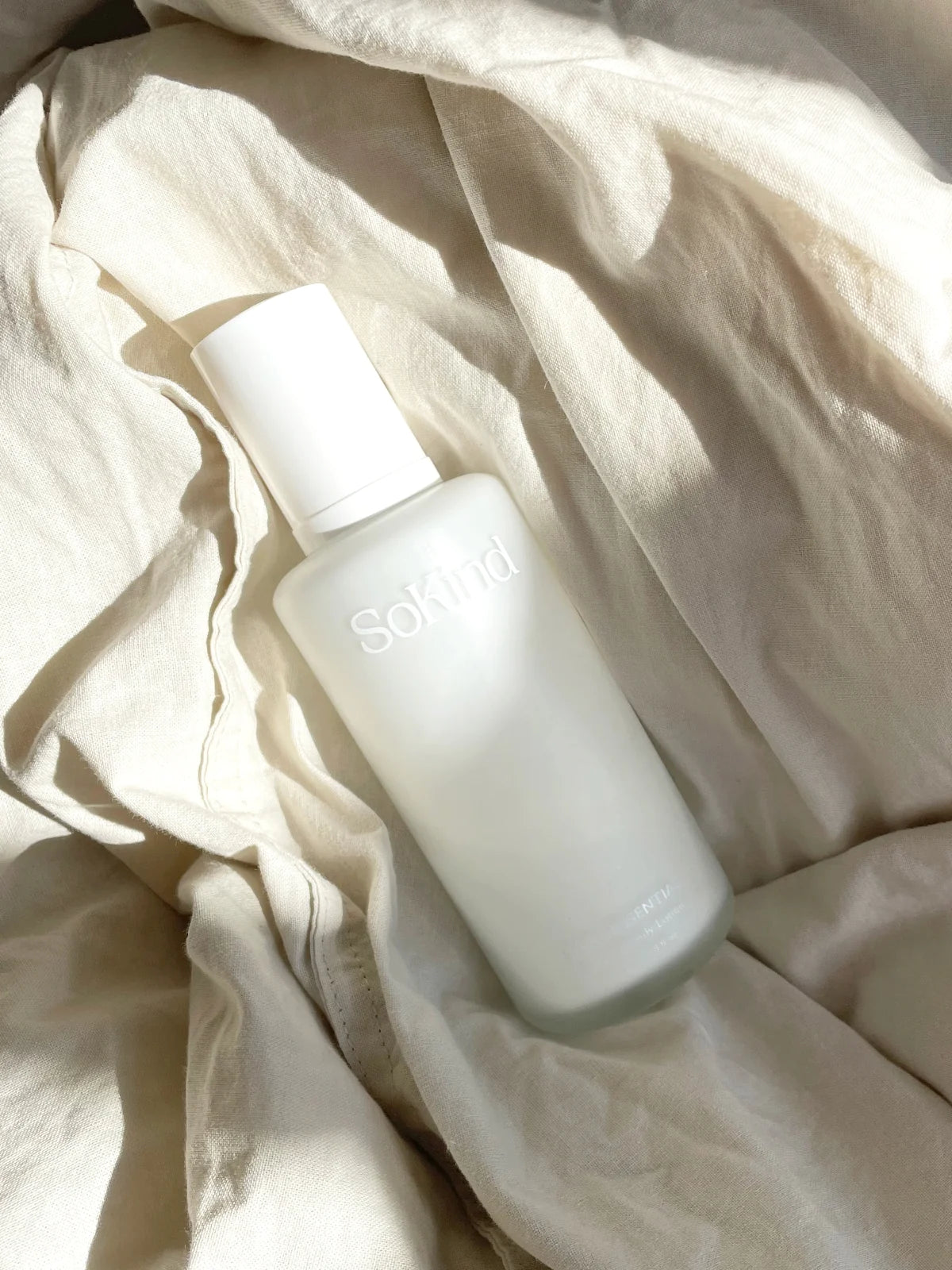 Silky Essential Body Lotion van SoKind in de zonnestralen op een beige doek.