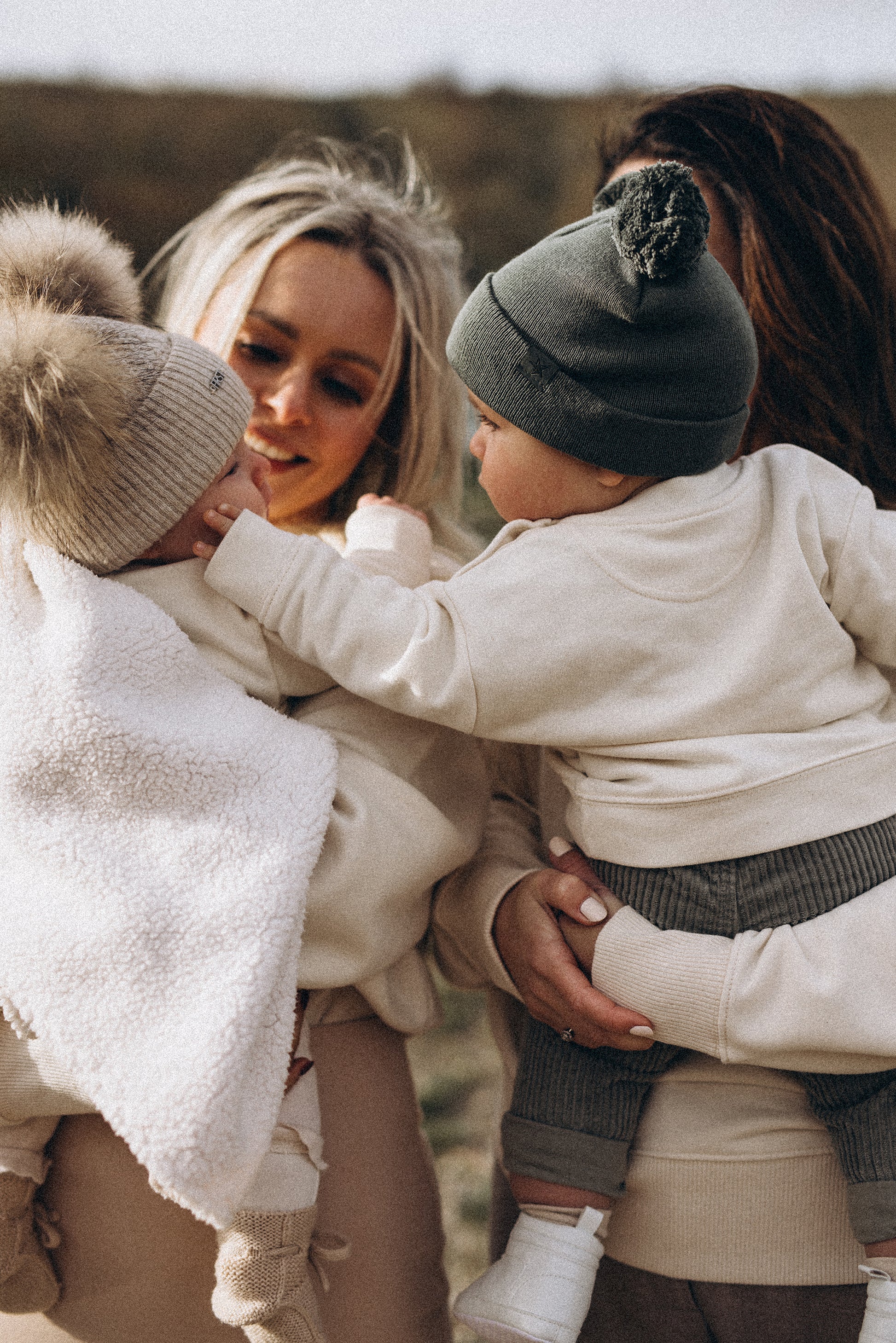Twee kindjes die de Kiddo of a Sad Beige Mom trui dragen worden gedragen door hun mama en raken elkaar aan.